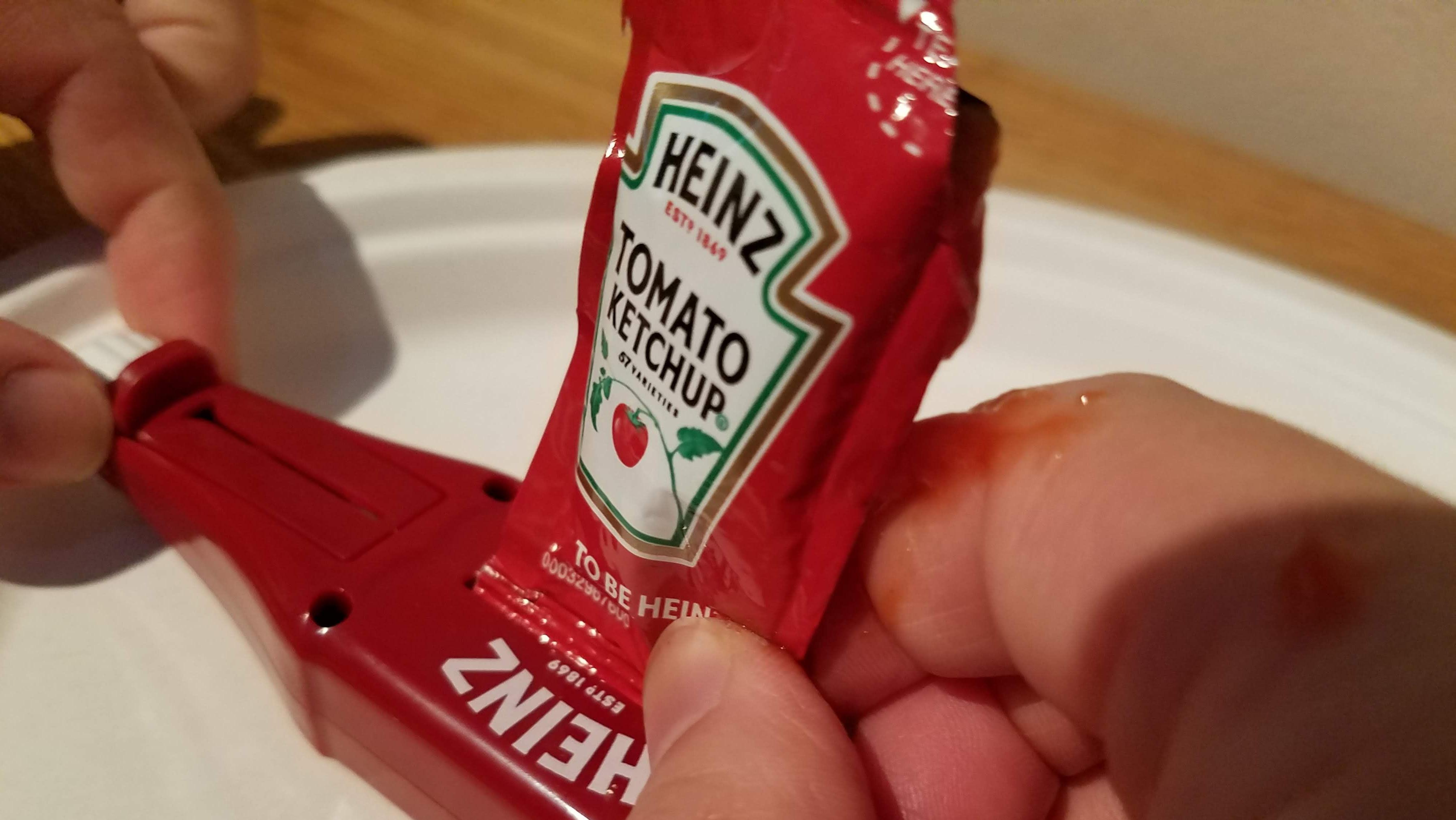 Placing a ketchup packet into the mouth of the Heinz Packet Roller