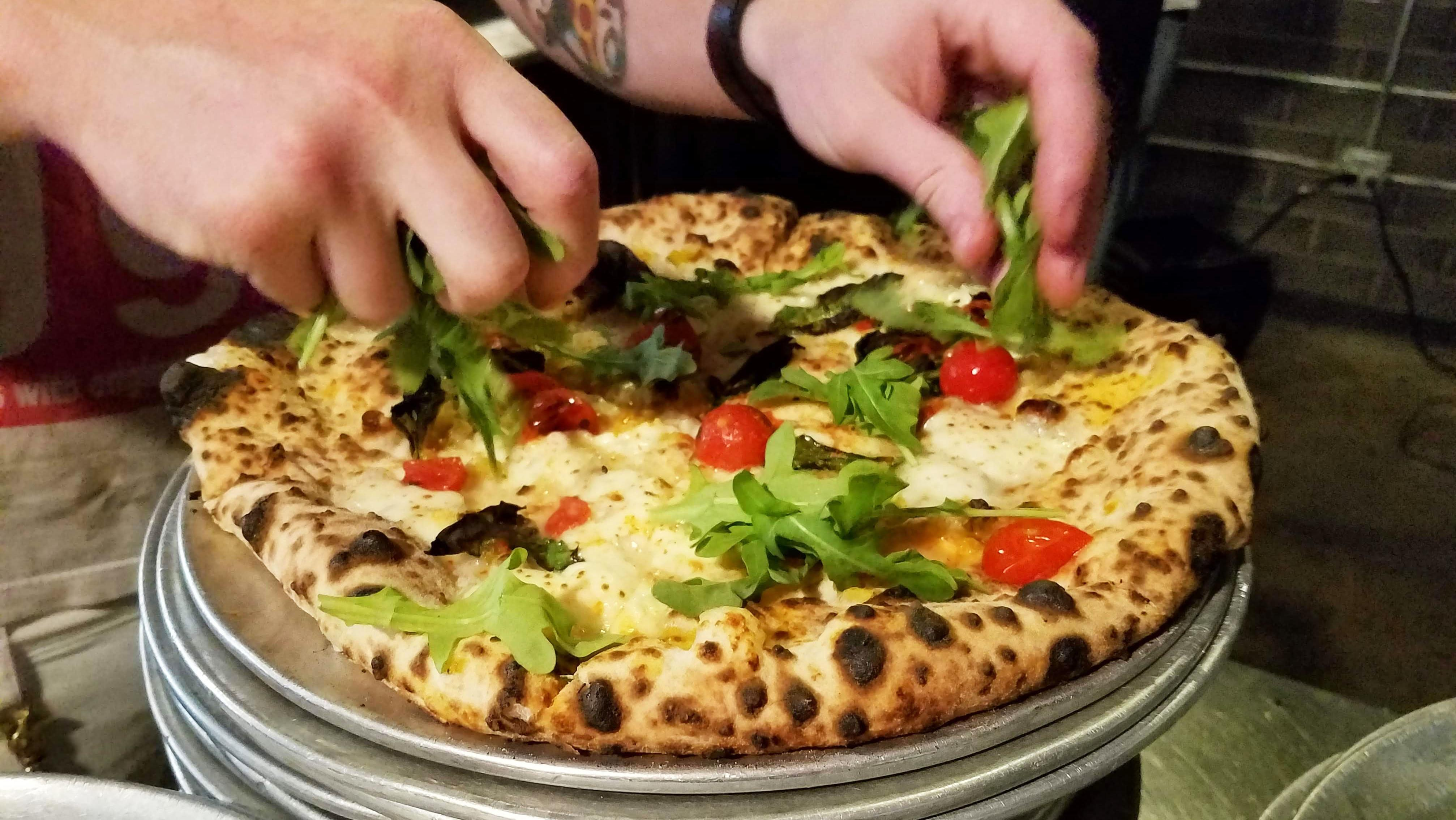 hands putting arugula on pizza