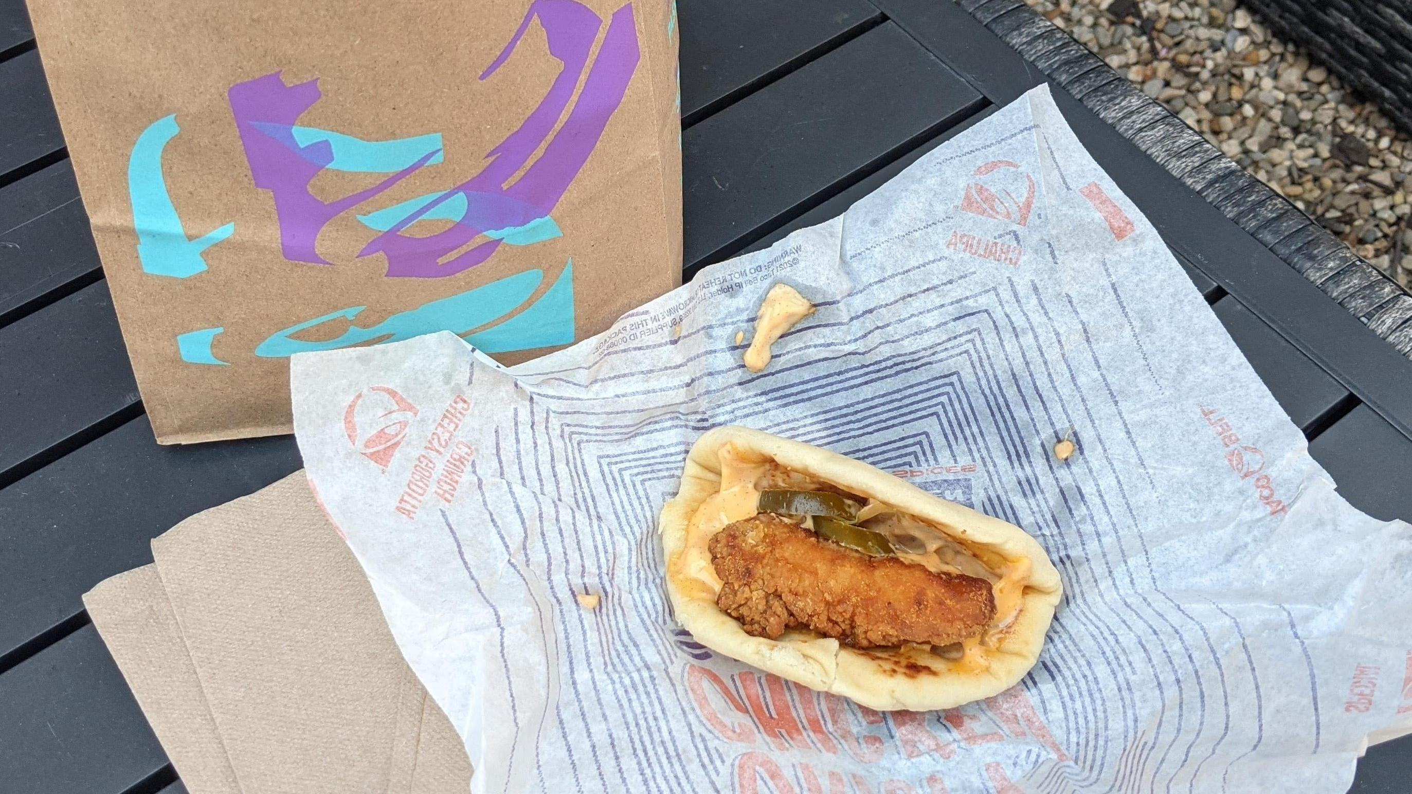 Taco Bell's new Crispy Chicken Sandwich Taco resting on wrapper beside Taco Bell bag