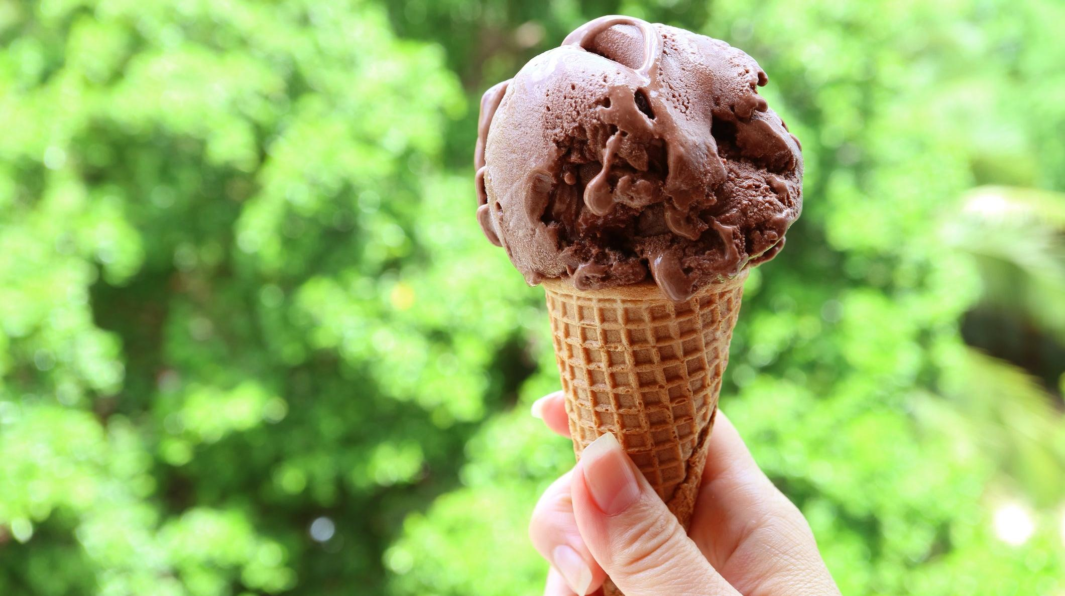 Hand holding scoop of chocolate ice cream perched on sugar cone
