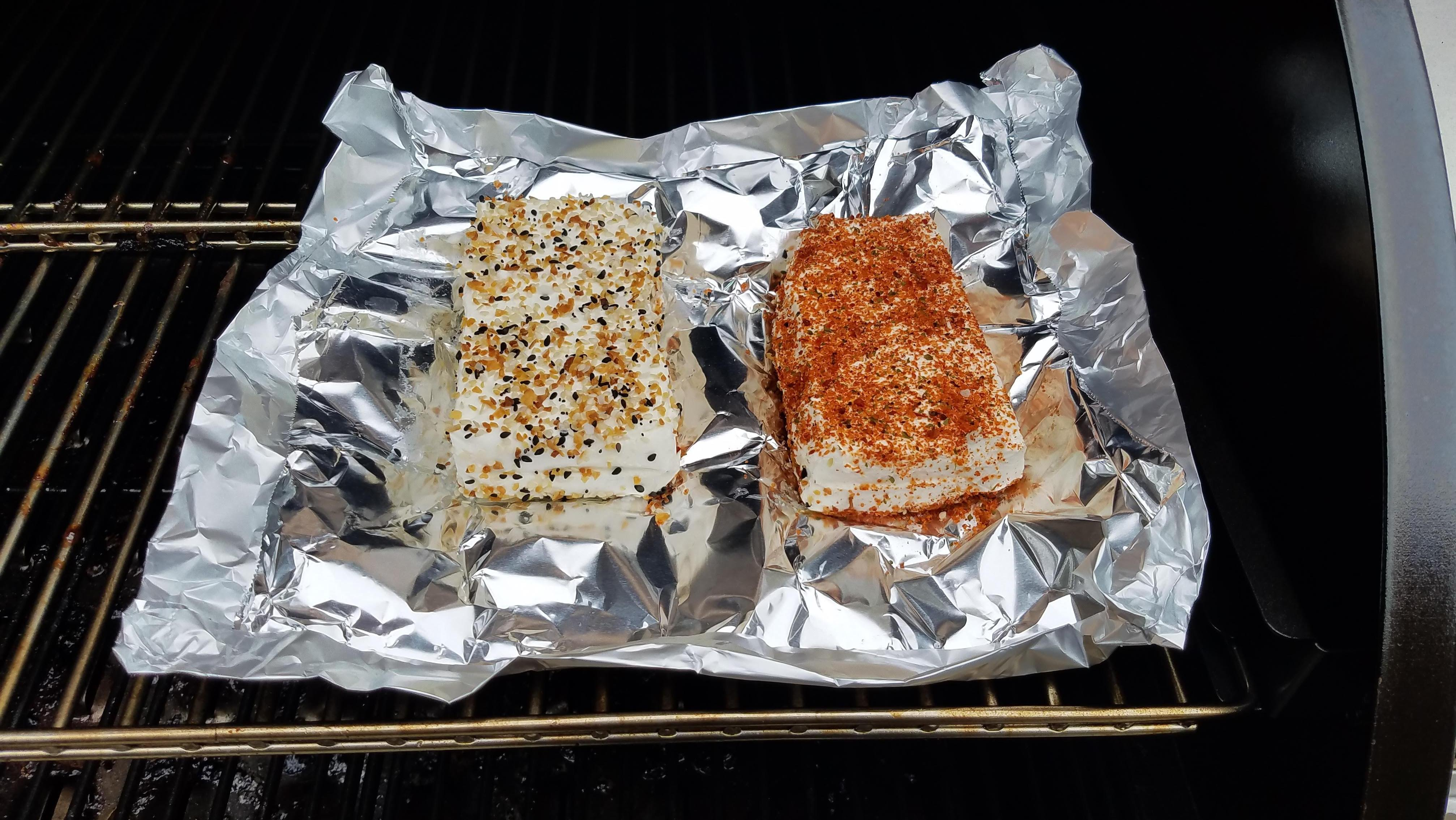 Two seasoned bricks of cream cheese on top of foil inside the smoker