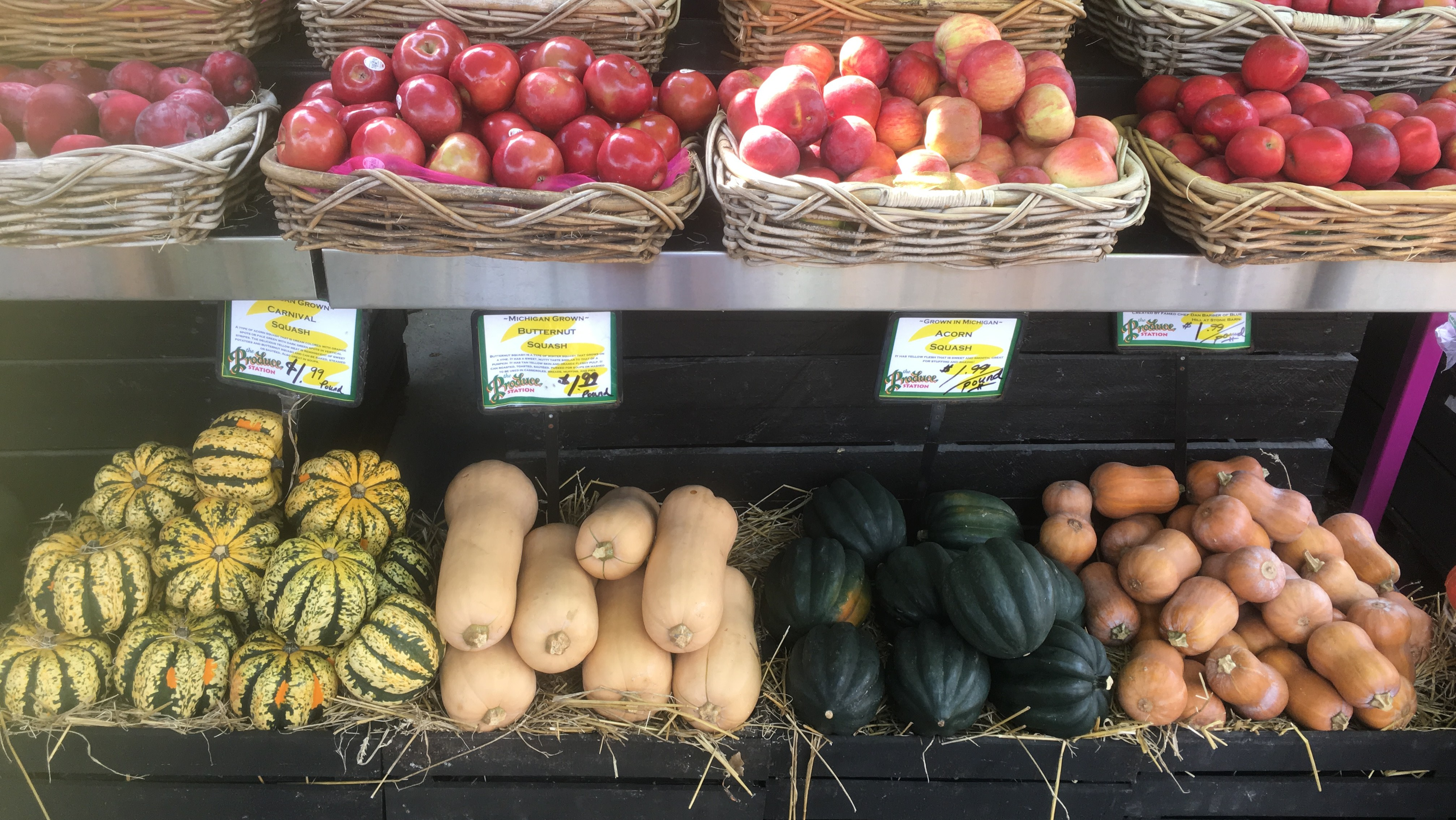 Baskets of produce at a farmers market, including butternut squash