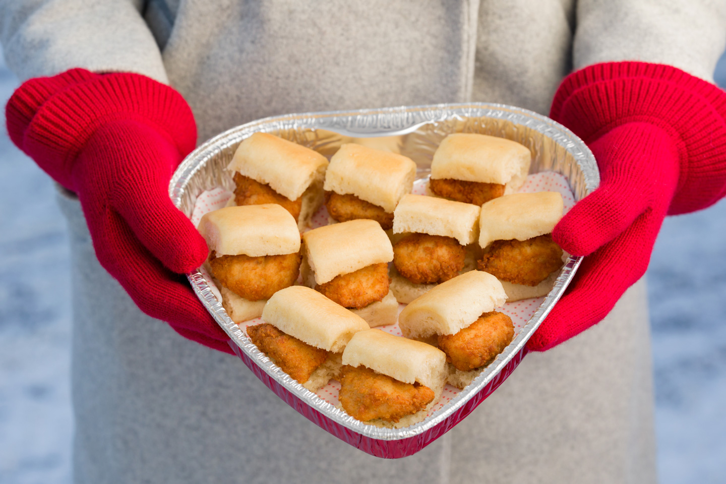 Woman in red gloves holds heart-shaped tin of mini chicken sandwiches