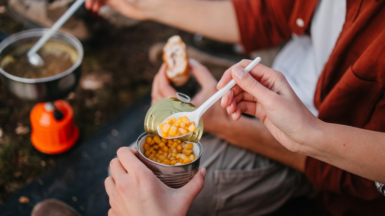 Hand scooping sweetcorn from a tin with a plastic spoon