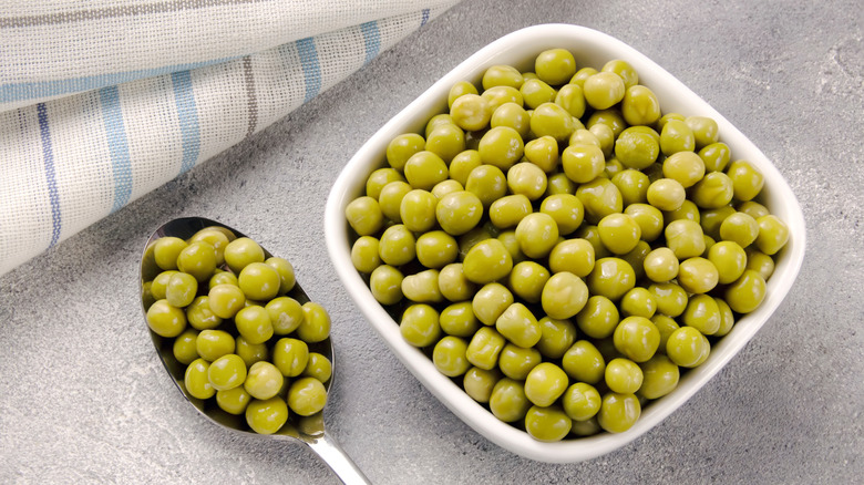 Spoonful of peas next to bowl of peas