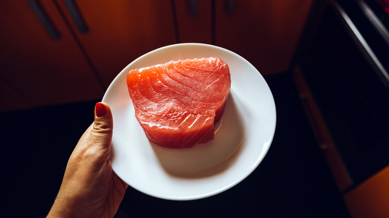 Person holding tuna steak on a plate