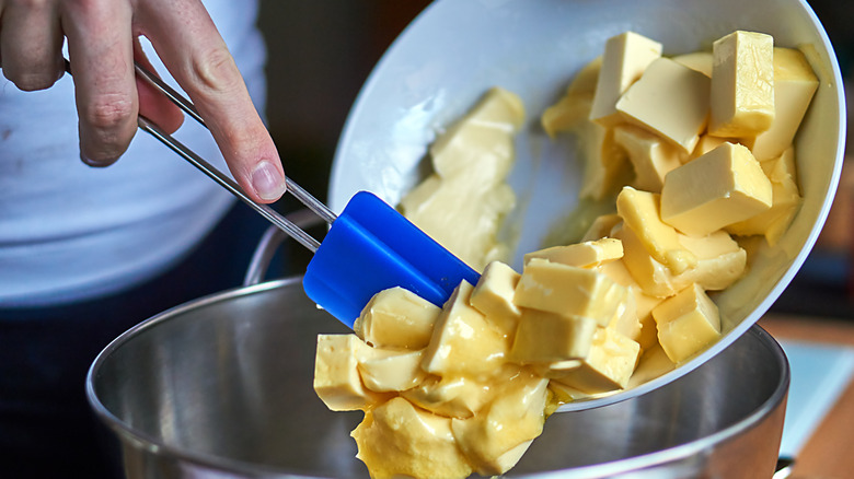 Hand spooning cubed butter into into a metal pan