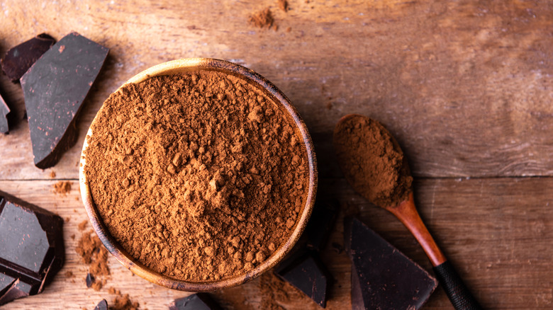 Bowl of cocoa powder on wooden table with dark chocolate and spoon