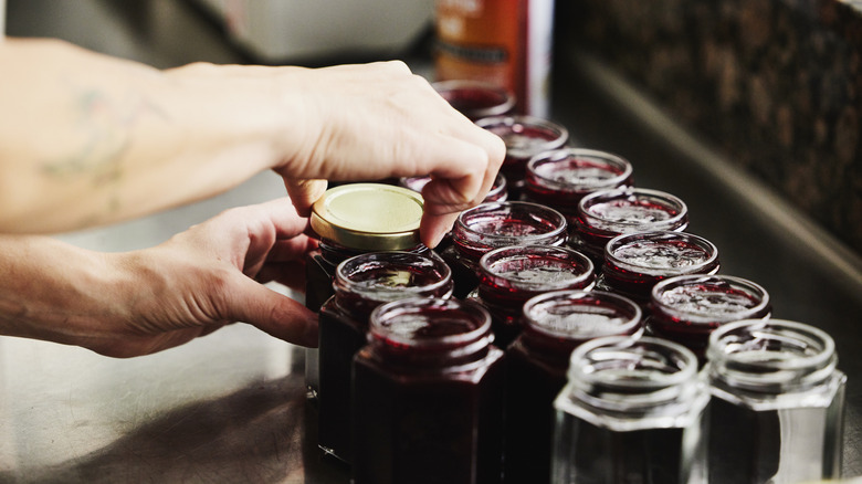 Hand opens one of many jars of fruit preserves