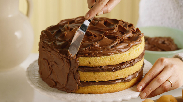 Hand spreading frosting onto cake