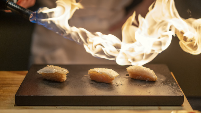 Blow torch emitting impressive flame over pieces of sushi