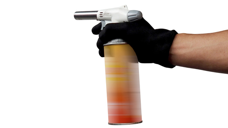 Gloved hand holding torch with gas canister against white background