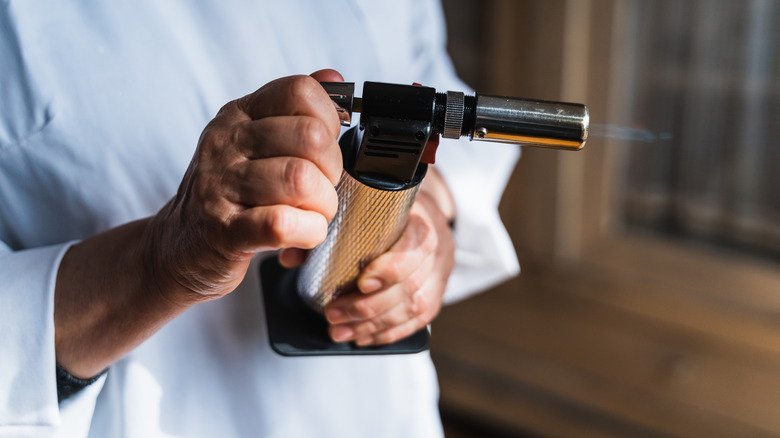 Close-up of chef's hands holding and tilting a kitchen torch