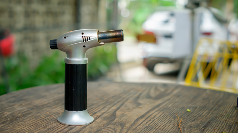 Culinary torch standing upright on wooden table outdoors