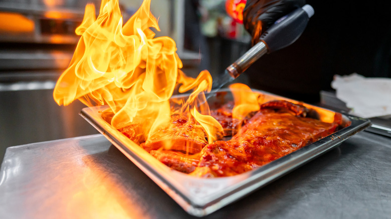 Chef using culinary torch to flame metal tray of ribs