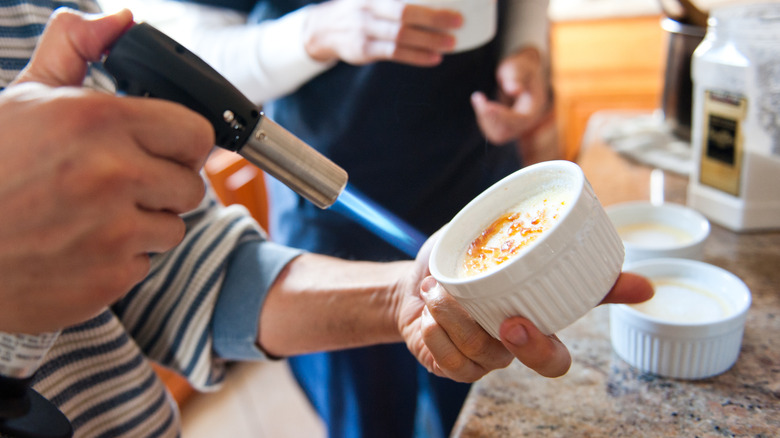 Woman's hands using culinary torch on ramekin of creme brulee