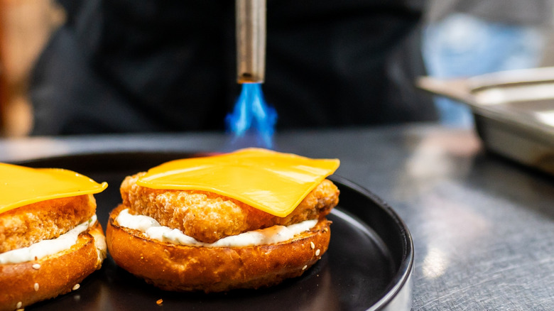 Culinary torching melting cheese over fried patty