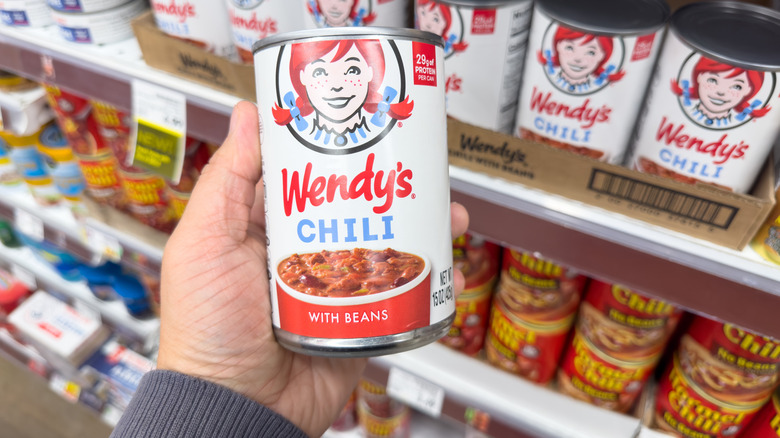 Handheld can of Wendy's chili in front of a grocery store shelf