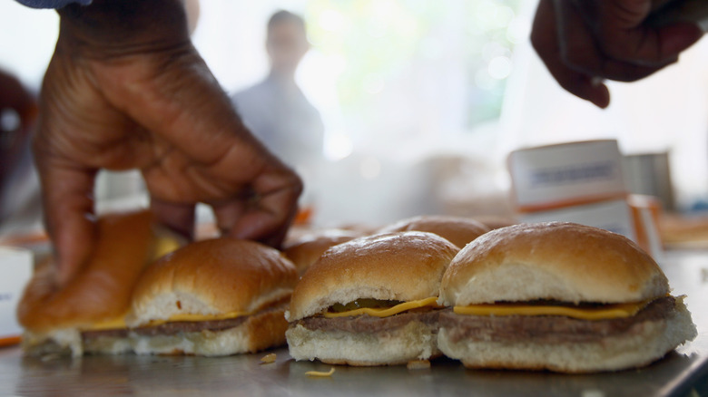 Two hands grilling and assembling a line of White Castle sliders