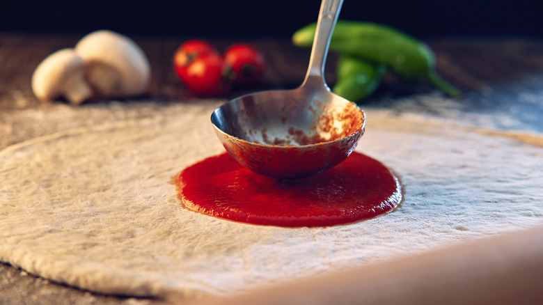 Pizza sauce being ladled on a pizza