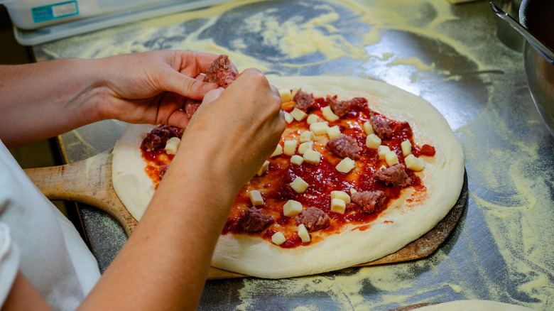 A chef applies toppings to a pizza