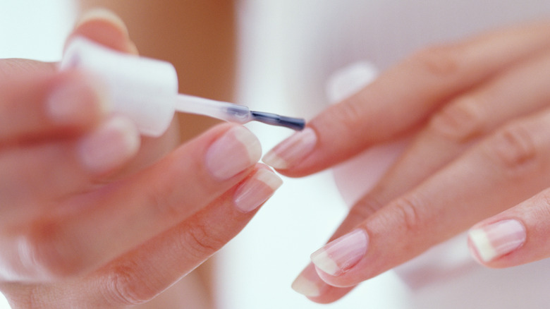 Hands painting nails with clear polish