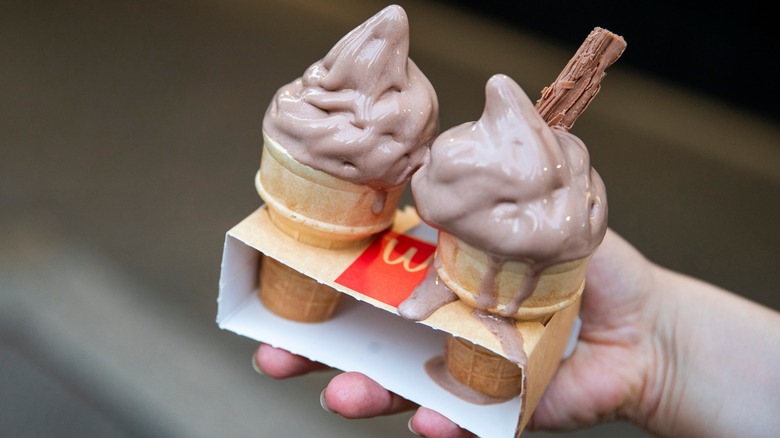 Hand holding two ice cream cones containing chocolate soft serve