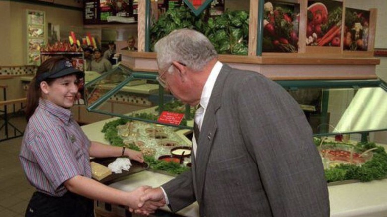 A Wendy's worker shakes hands with a man in a suit in front of the Wendy's salad bar