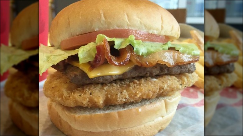 Burger stacked with chicken, beef, and bacon