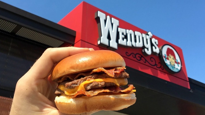 Hand holding a Baconator in front of Wendy's