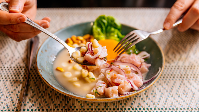 Hands with fork and spoon tucking into ceviche