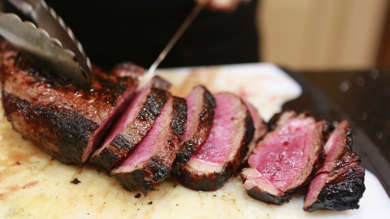 Knife cutting up medium rare steak