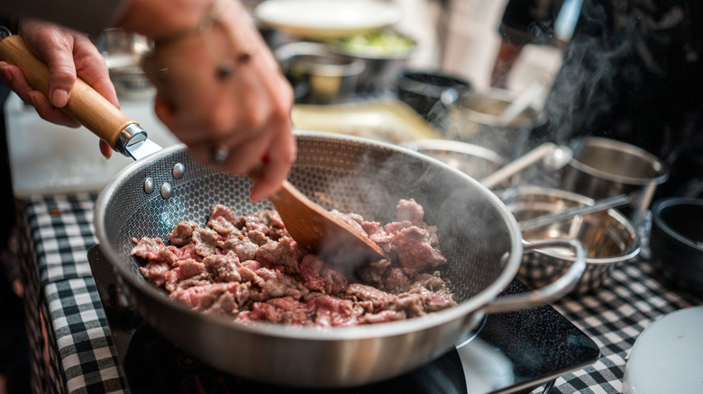 Hands cooking ground beef in frying pan