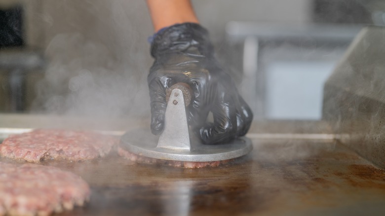 Person pressing a patty on a griddle