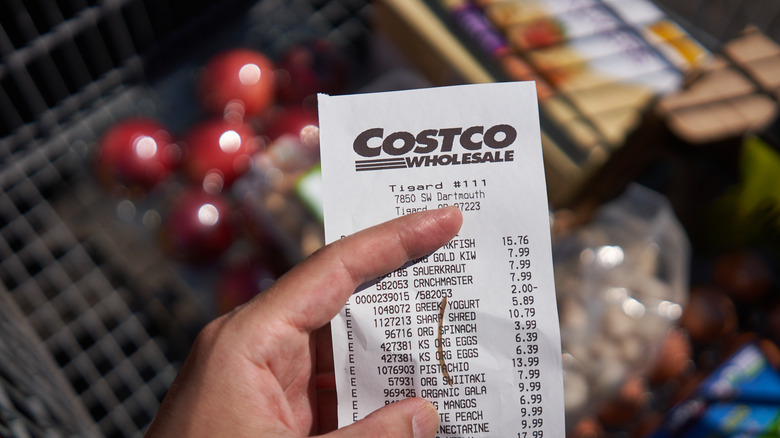 Hand holding Costco receipt above cart