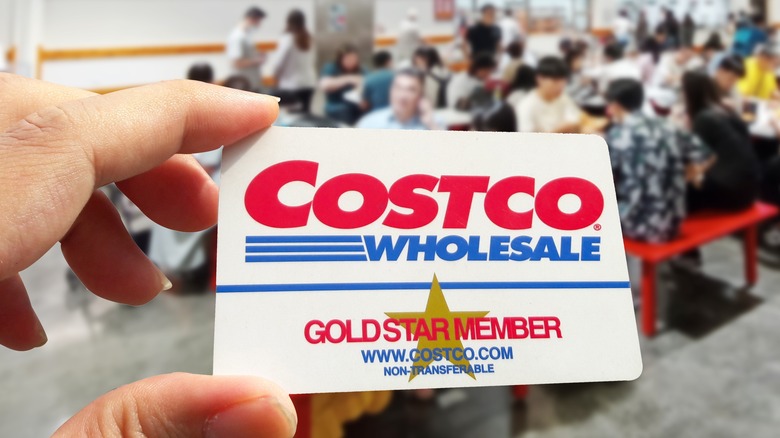 Hand holding Costco membership card with food court in backdrop