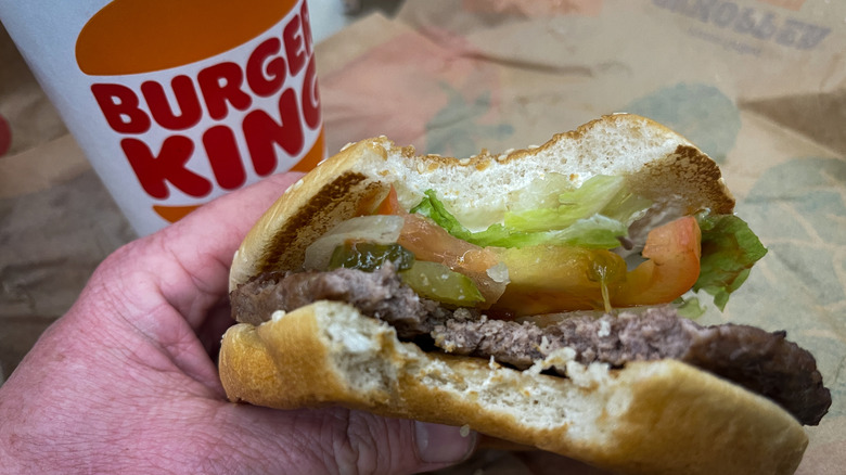 Hand holding Whopper burger next to drink