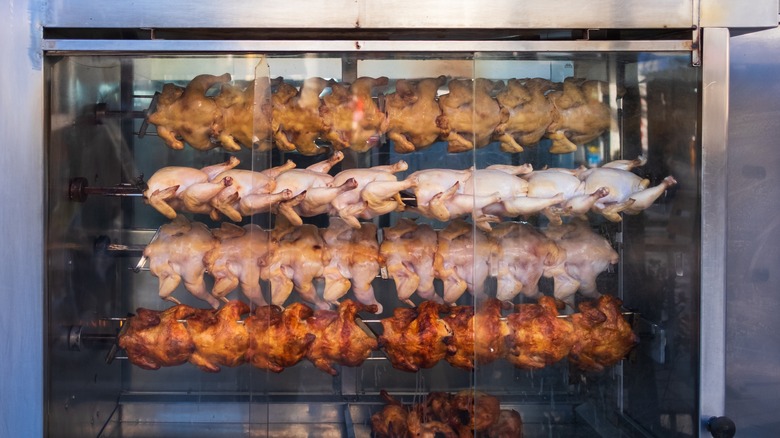 Four rows of rotisserie chickens being cooked