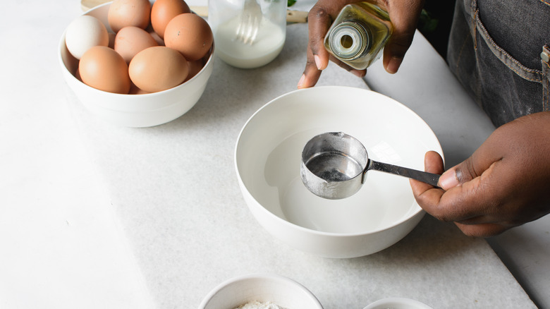 Pouring oil into measuring cup over a white bowl