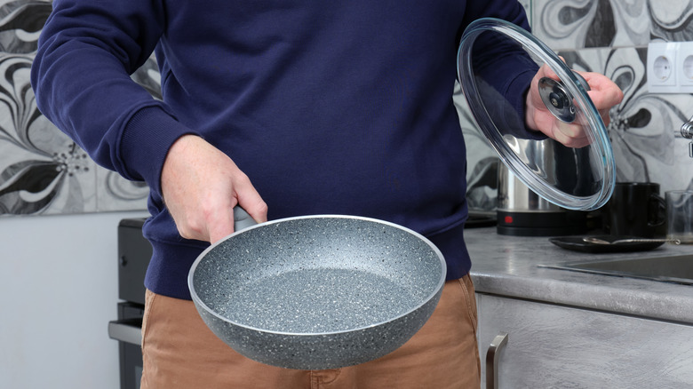 Person in kitchen holding frying pan and lid