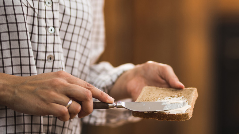 Person holding and buttering bread slice