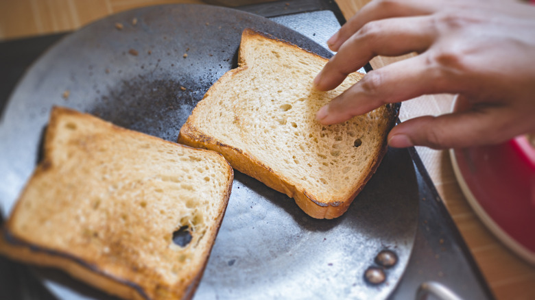 Person toasting bread slices on frying pan