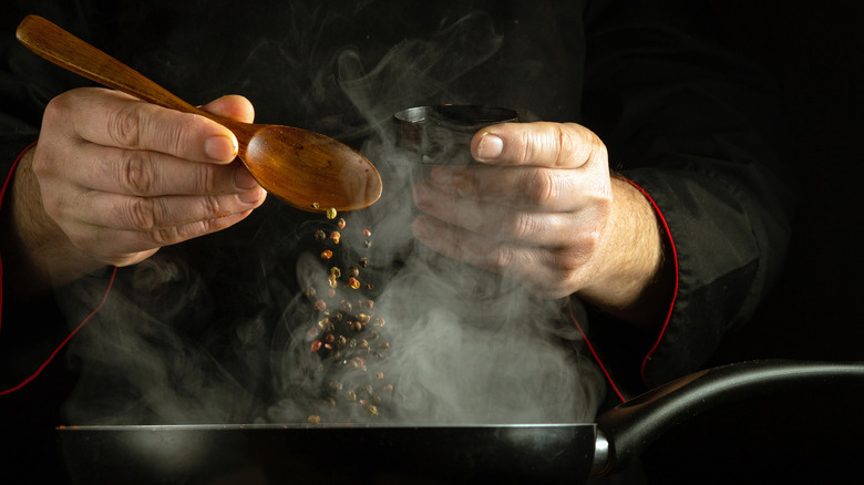 Chef sprinkles peppercorns onto frying pan