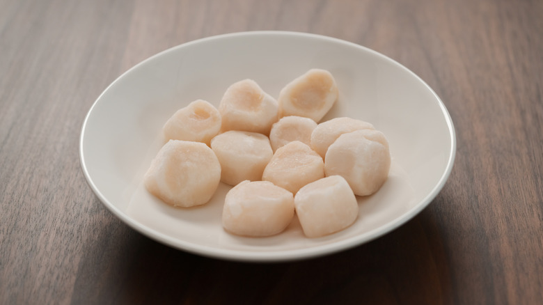 Frozen scallops thawing in white bowl on wooden counter