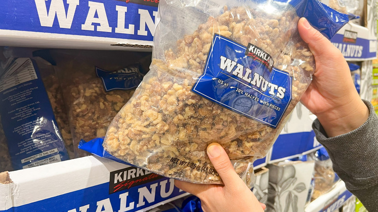 Person grabbing Kirkland walnuts off store shelf