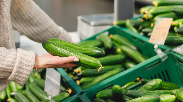 Person selecting cucumbers from a grocery store bin