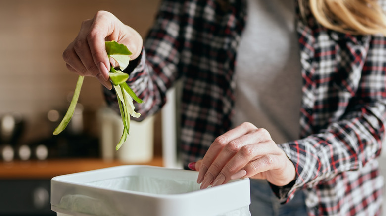 A person throwing away cucumber peels into a white compost bin