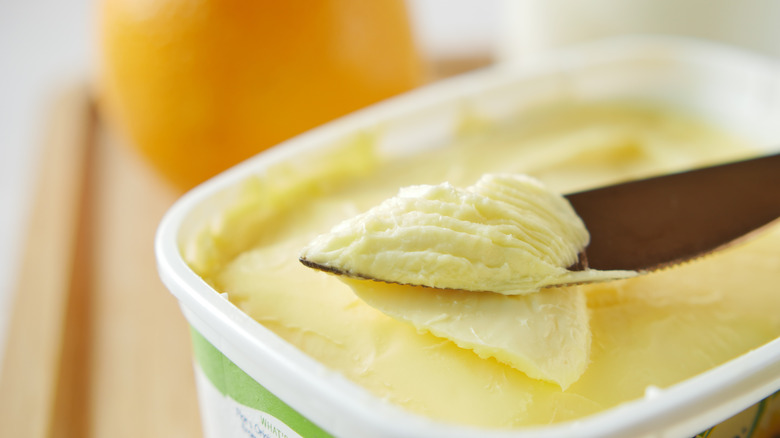 Knife cutting into margarine in a tub