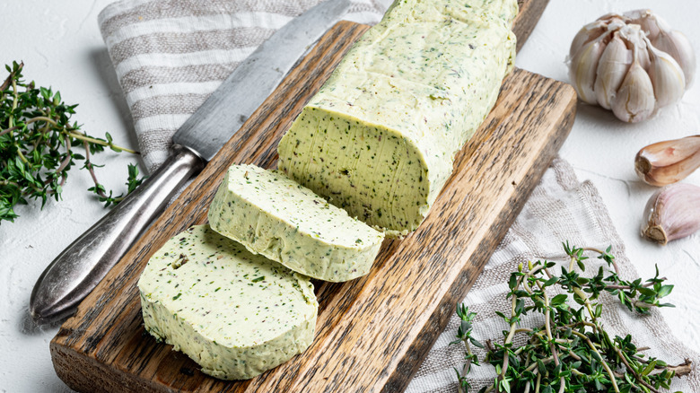 Compound butter on a wooden block surrounded by herbs and garlic