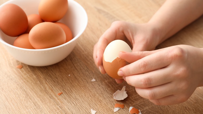 hands peeling hard boiled eggs